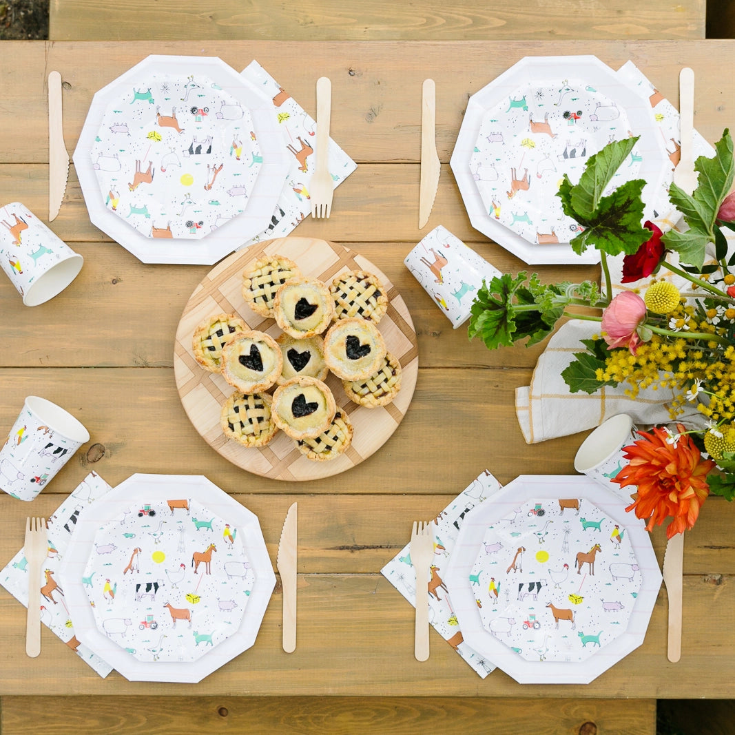 Outdoor picnic table set with farm‑animal cups, octagon plates, and mini pies for a kids’ barnyard birthday.