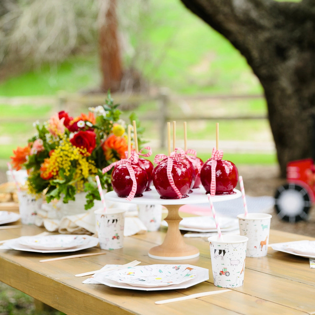 Dessert table with candied apples and cups, farm animal plates beneath on wooden table.