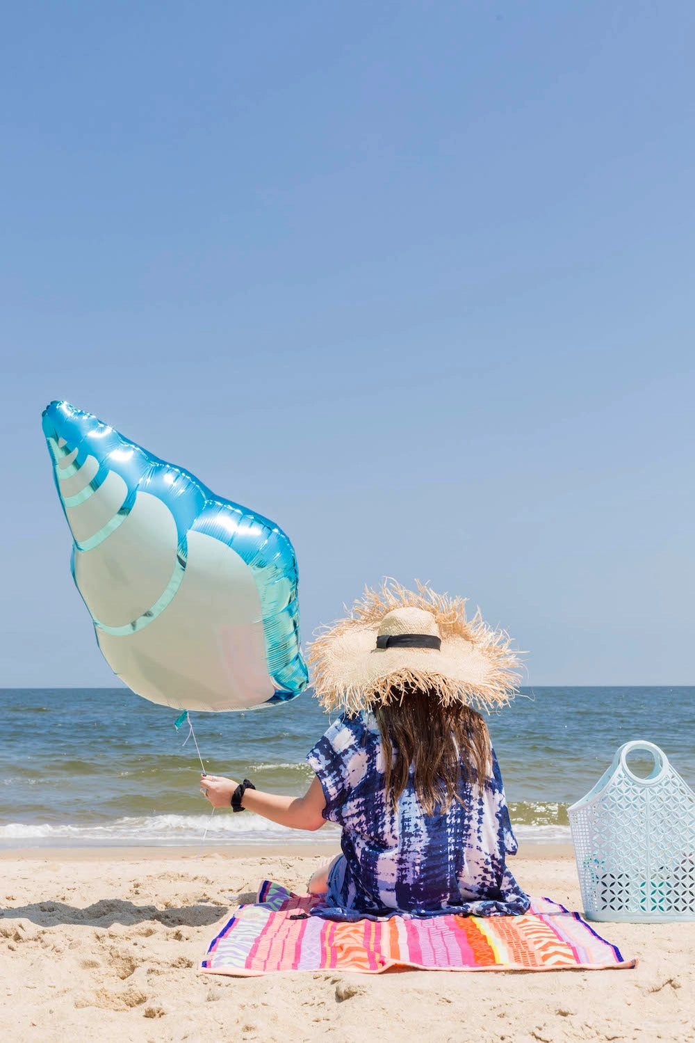 Sea shell mylar balloon floating beside a woman on the beach—perfect for ocean or mermaid party photo ops.