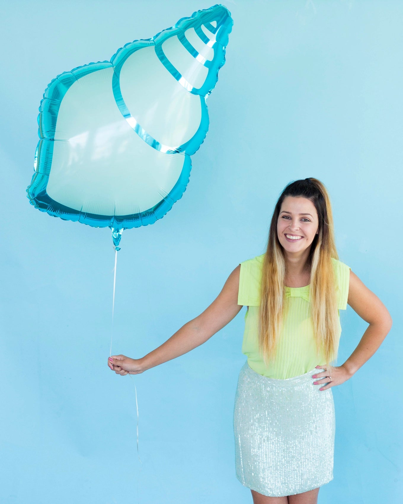 Woman holding a large blue sea shell mylar balloon, ideal for ocean or mermaid-themed birthday party decorations.