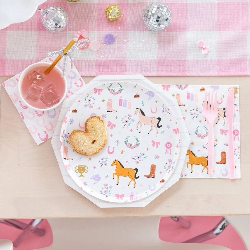 Octagon plate with horse and floral print sitting on a larger white plate; heart‑shaped pastry and pink drink rest on top of a horseshoe napkin.