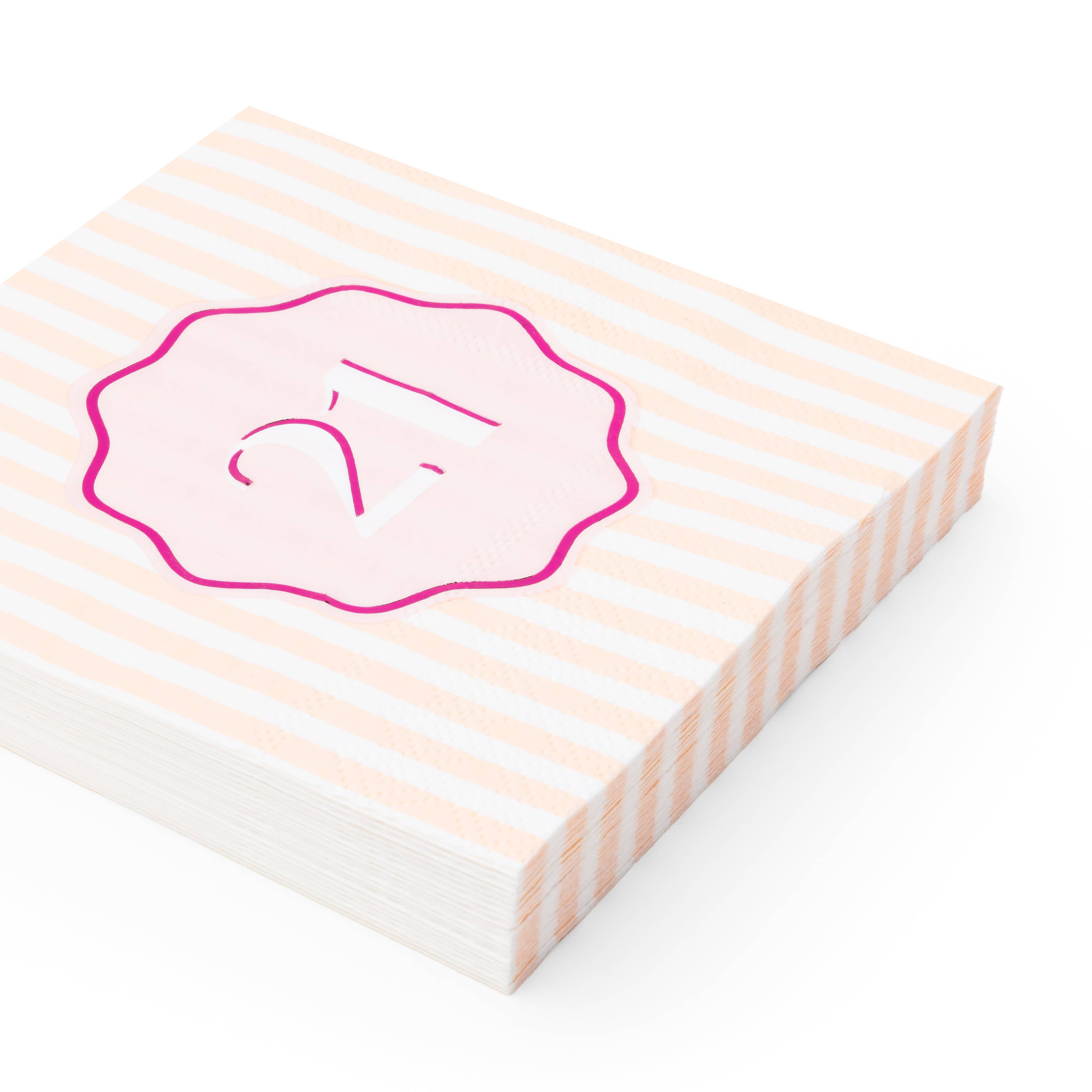 Angled stack of peach and white striped 21st birthday cocktail napkins with pink foil number badge
