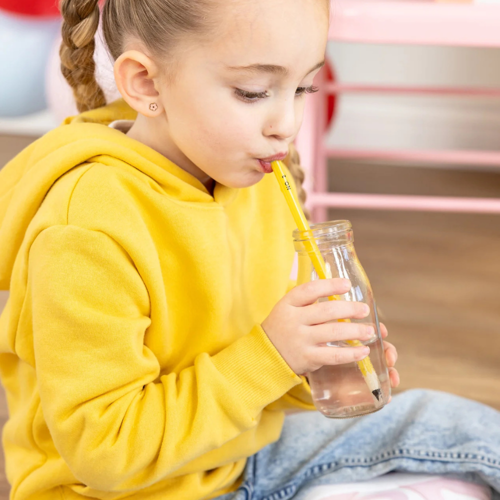 Child drinking from a pencil-themed straw in a clear glass bottle