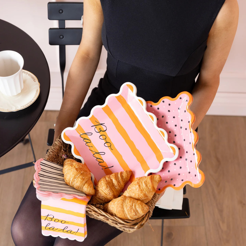 Basket of Boo La La plates and napkins filled with croissants on a woman's lap.