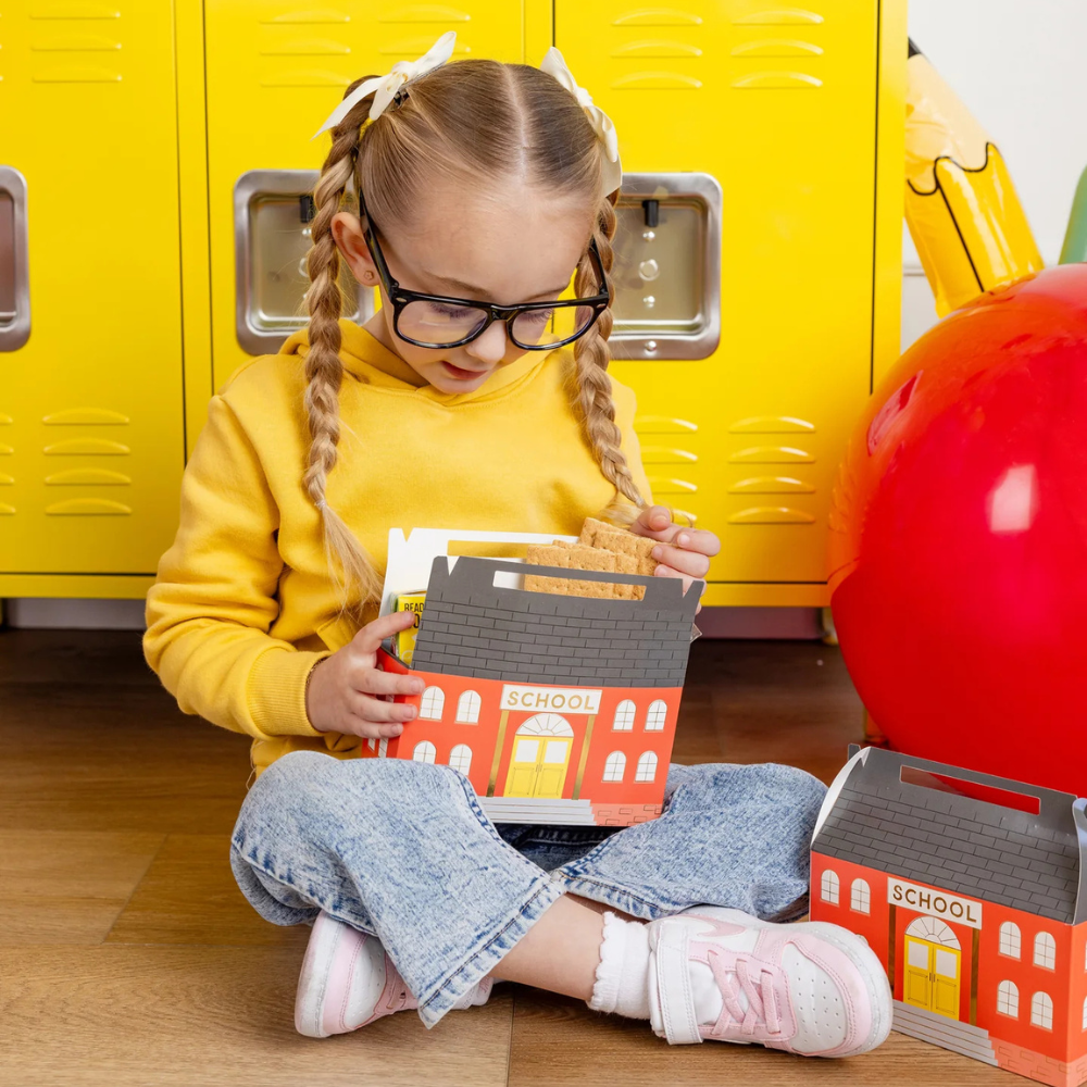 Child in yellow sweatshirt holding a filled schoolhouse treat box in front of lockers