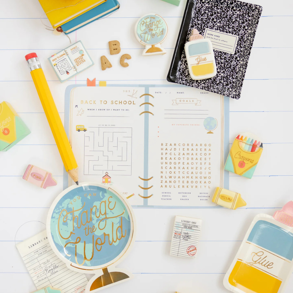 Flat lay of a back to school setup featuring notebooks, cookies, pencils, and a library card napkin near themed paper goods.