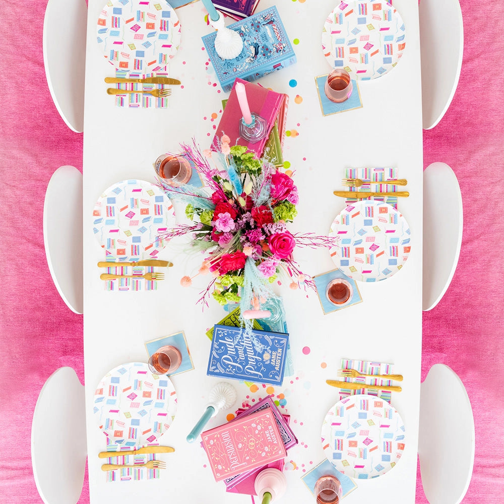 Bright book club table with vibrant floral centerpiece, book plates, teal coasters, and bookshelf napkins at each place.