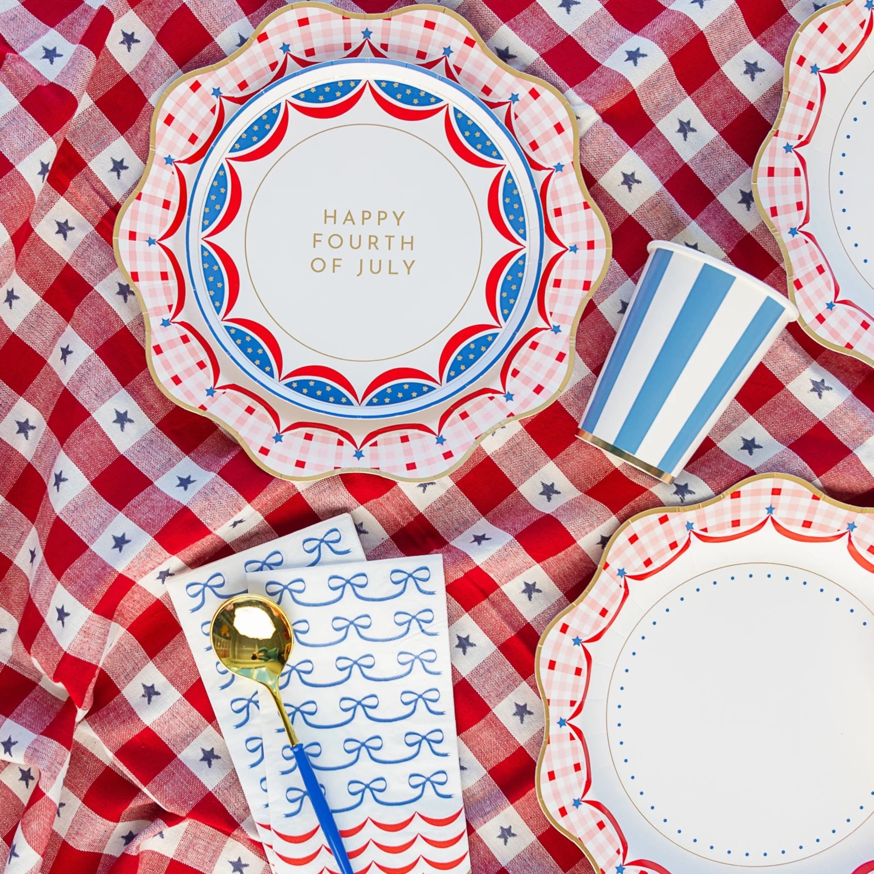 A set of 4th of July guest towels styled with blue and white striped cups, gold flatware, and a red gingham tablecloth, creating the perfect patriotic party setup.