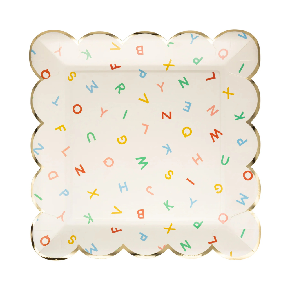 Flat lay of square paper plate with scattered colorful letters and scalloped gold foil edges