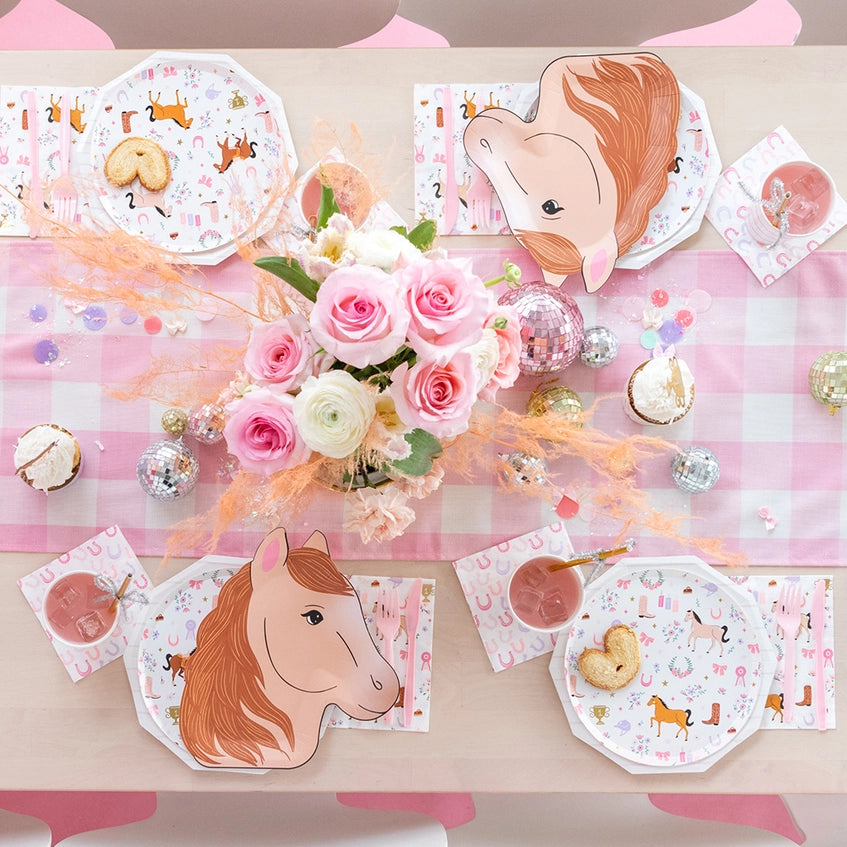 Overhead view of pink gingham table set with pony‑shaped plates, octagon horse‑pattern plates, roses, and mini disco balls.