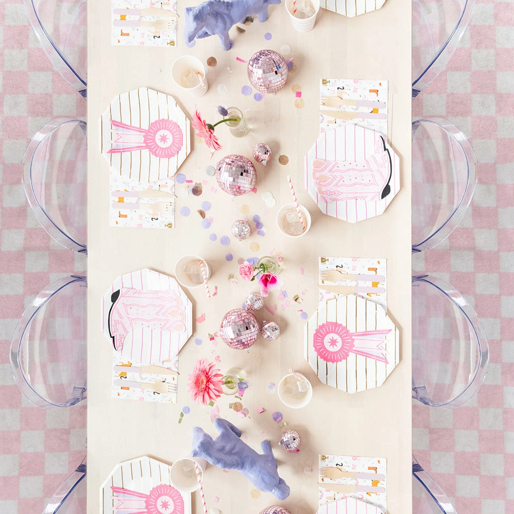 One large square napkin on a white background, printed with pastel-pink and lavender show ribbons, roses, horseshoes, tan and brown prancing horses, a gold trophy, floral wreaths, and tiny cowgirl boots.
