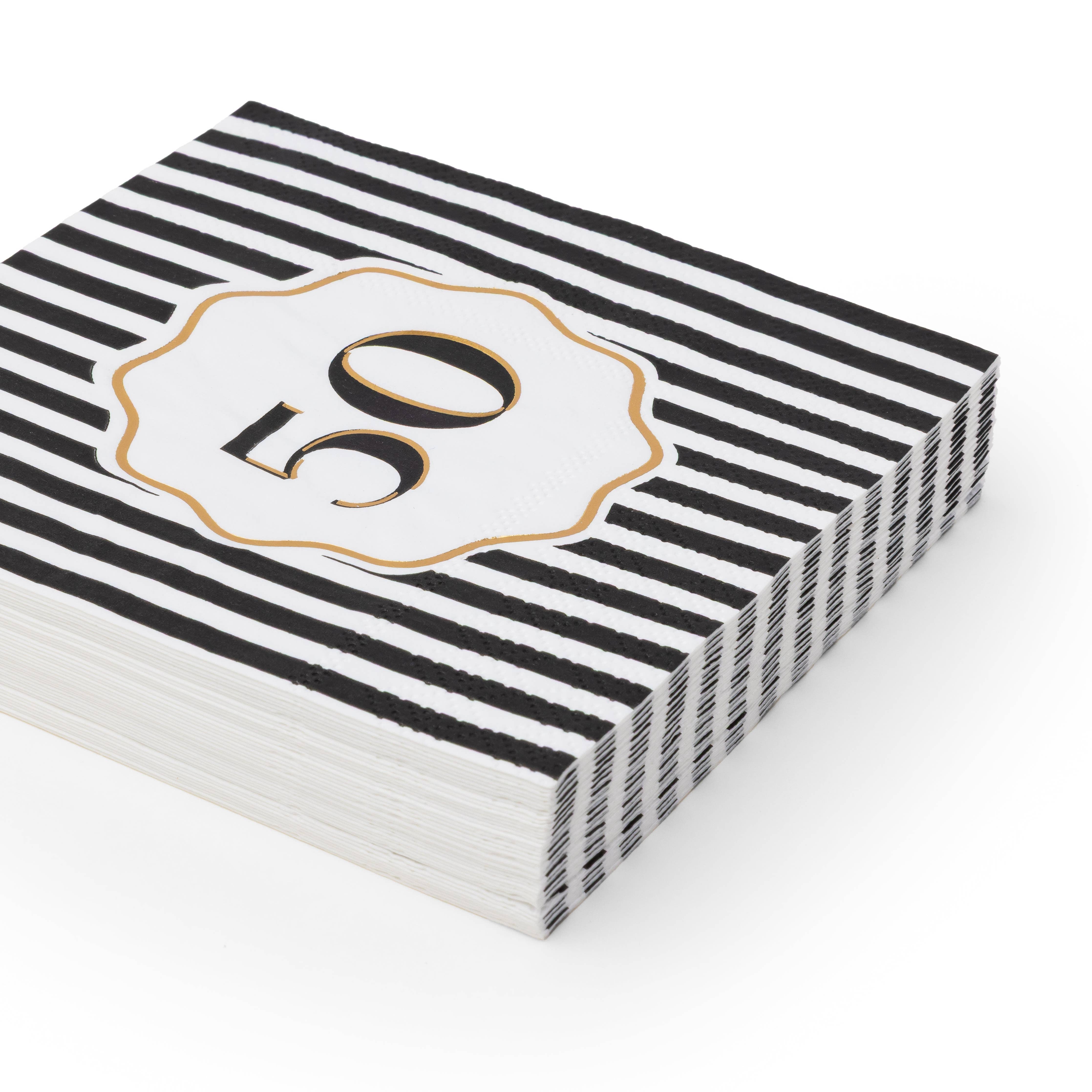 Angled stack of black and white striped 50th birthday cocktail napkins with white gold foil number 50 scalloped medallion on white background