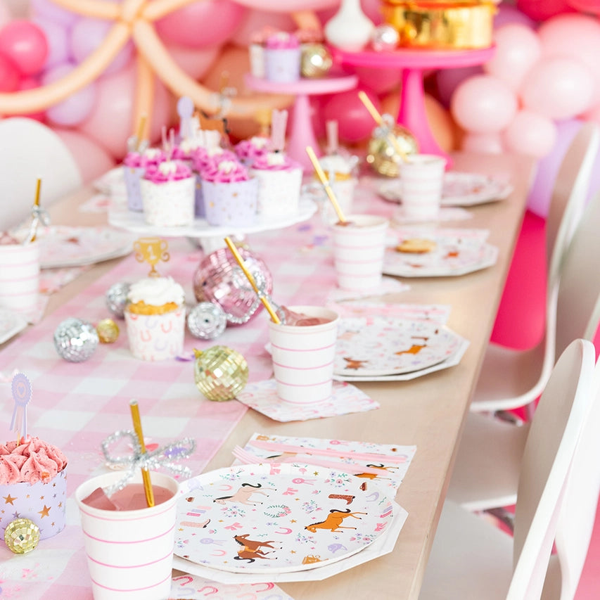  Long pink‑and‑white gingham runner with pony‑print plates, striped cups, disco‑ball accents, and horseshoe napkins under each place setting.
