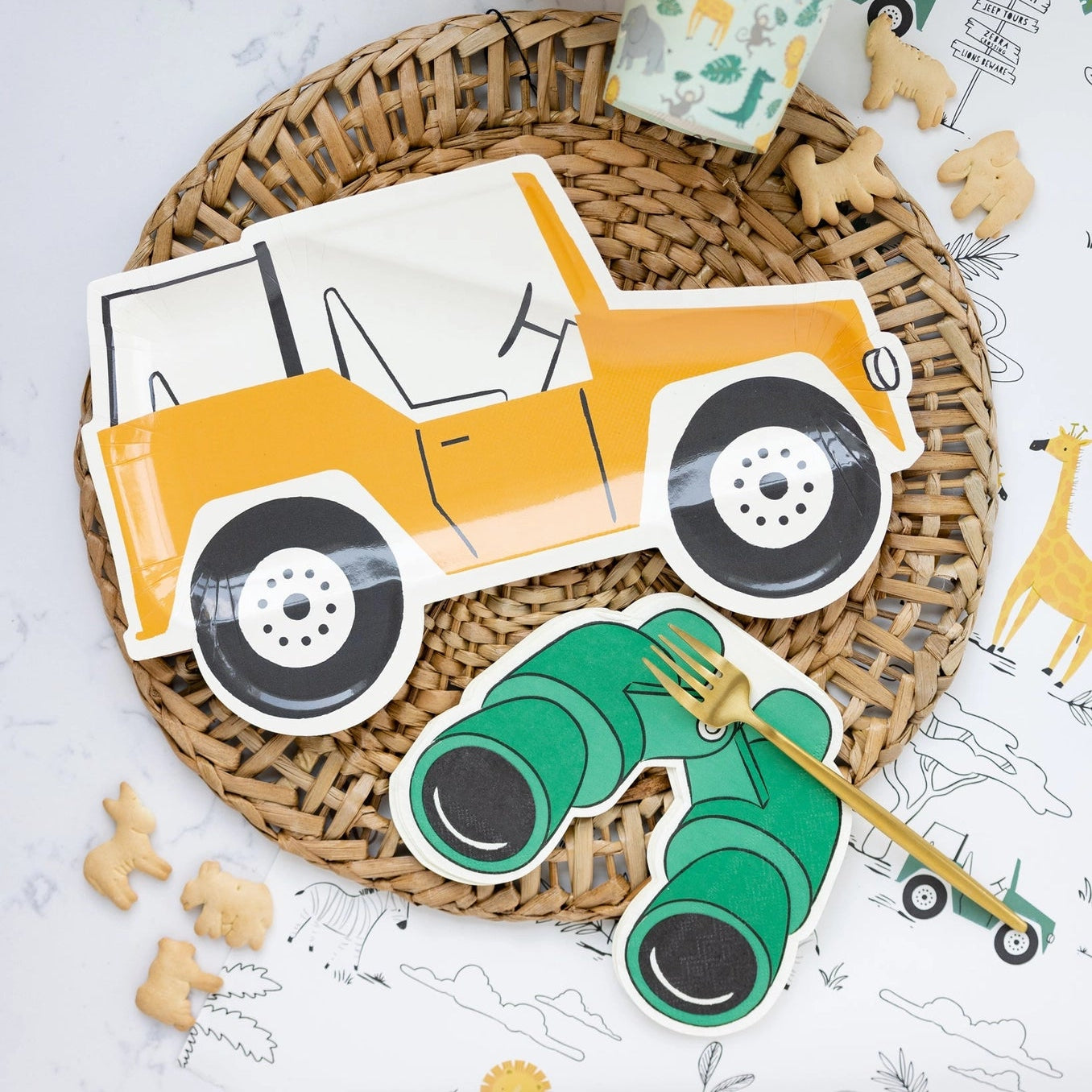 Safari-themed party setting featuring binocular-shaped paper napkins, safari Jeep plates, animal cookies, and patterned cups.