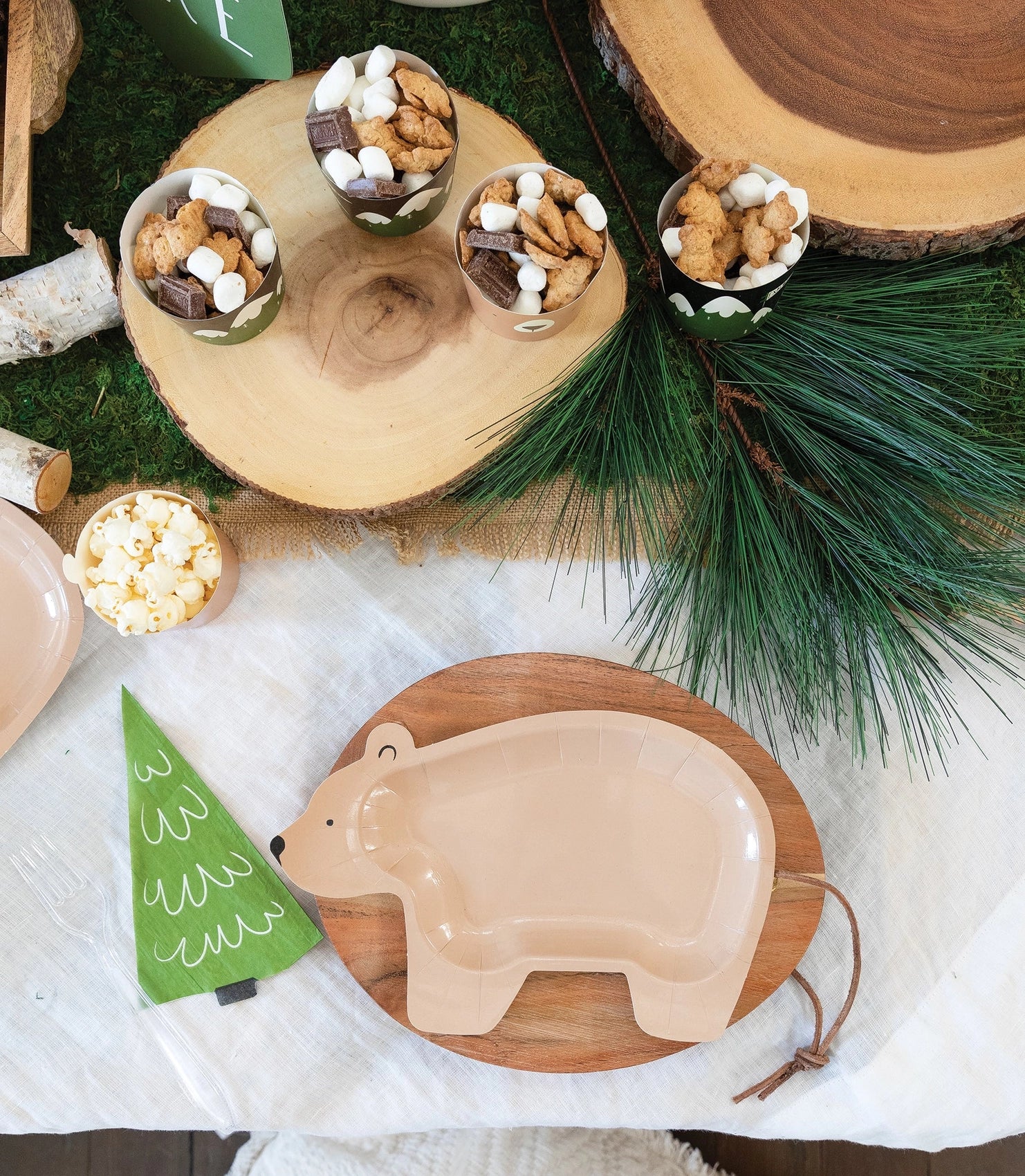 Bear plate placed on a wood slice charger with green pine tree napkin and party snacks surrounding it