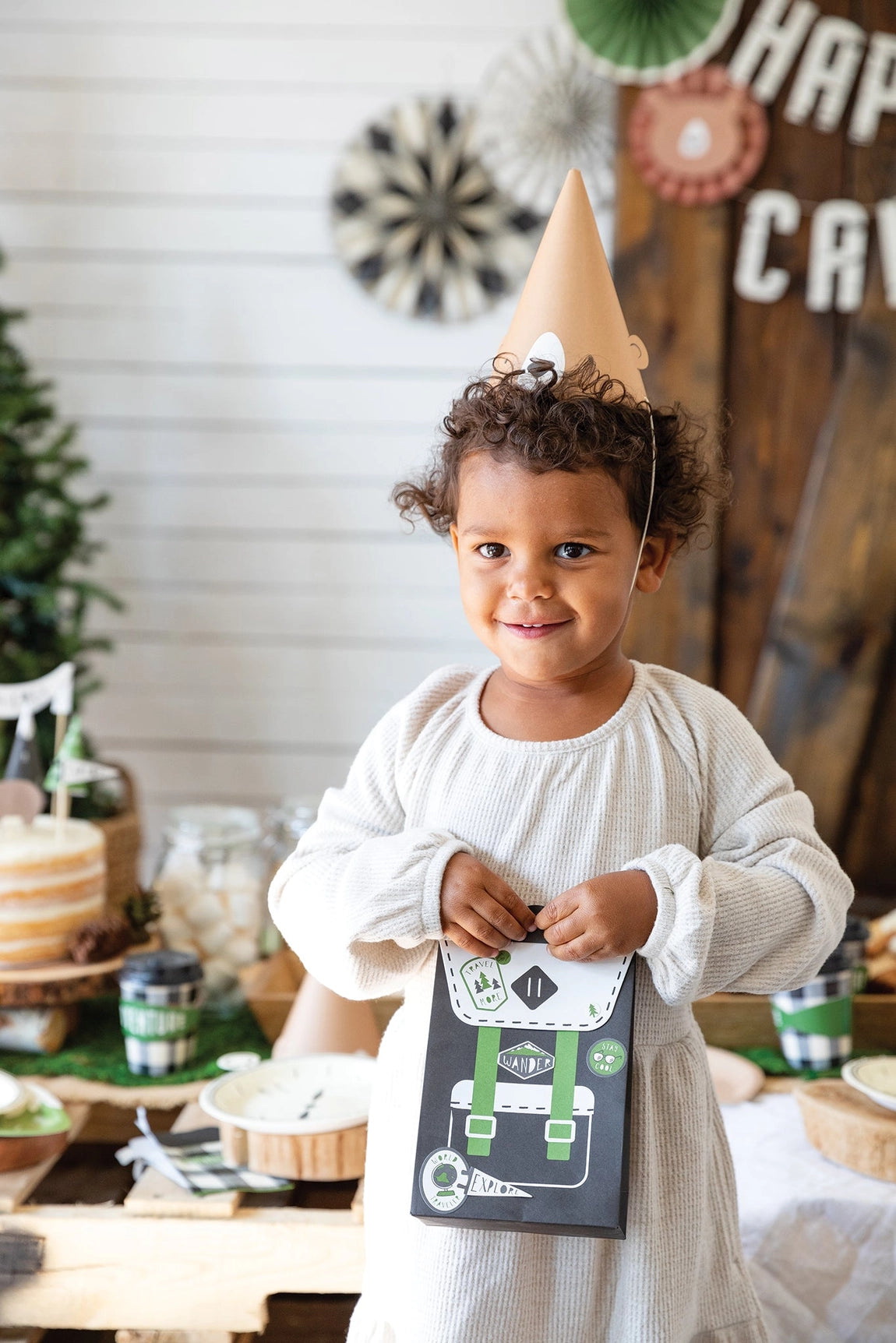 Themed birthday scene with paper backpack favor bags, a bear snack cup, and green plaid coffee cups—all styled for an outdoorsy kid’s party.