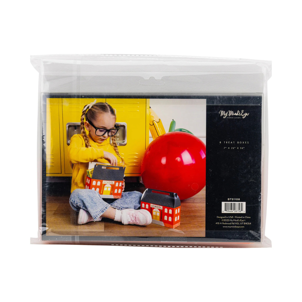 Young girl in glasses sitting on the floor opening a schoolhouse-shaped treat box