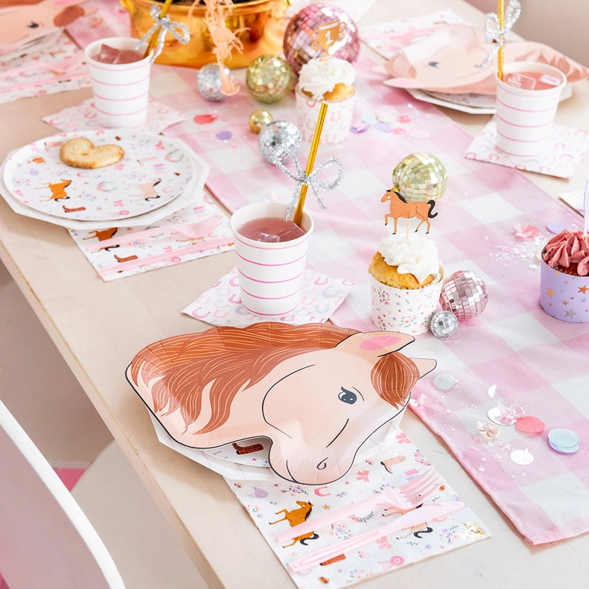 Angled shot of party table featuring striped cups, pony dinner plate, cupcakes, and glittery horseshoe décor.