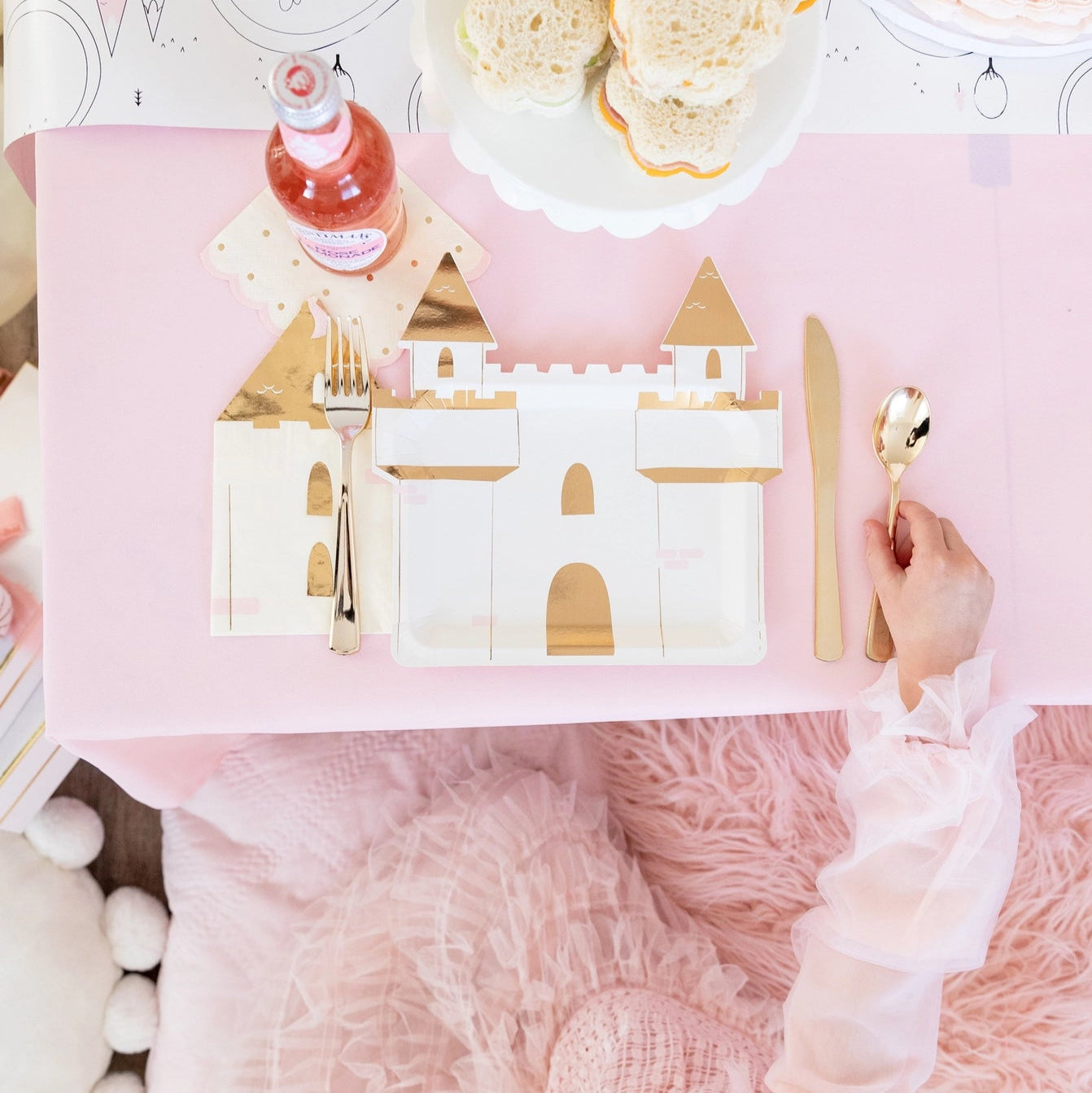 Overhead shot of pink table set with gold-foil castle napkins used as place mat for matching castle plate and gold cutlery at princess party.