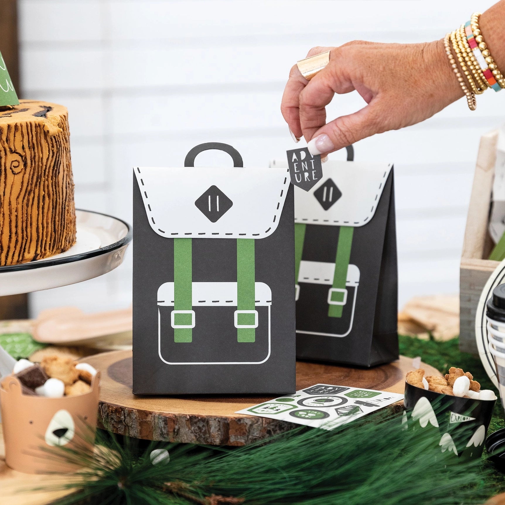 Flat lay of all 8 paper favor bags and 8 included sticker sheets with adventure and wilderness-themed icons.