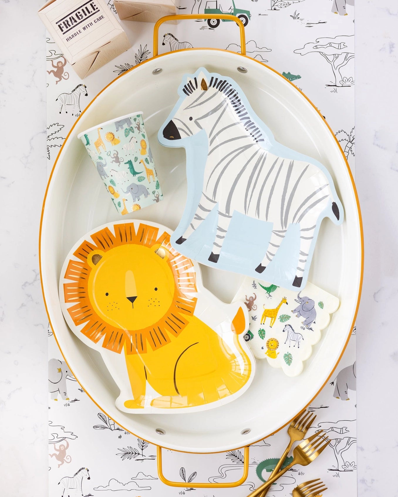 A vibrant arrangement showcasing playful lion and zebra-shaped plates, animal-themed cups, and charming cocktail napkins on a chic white tray with gold accents, perfect for a kid's jungle or safari-themed party.
