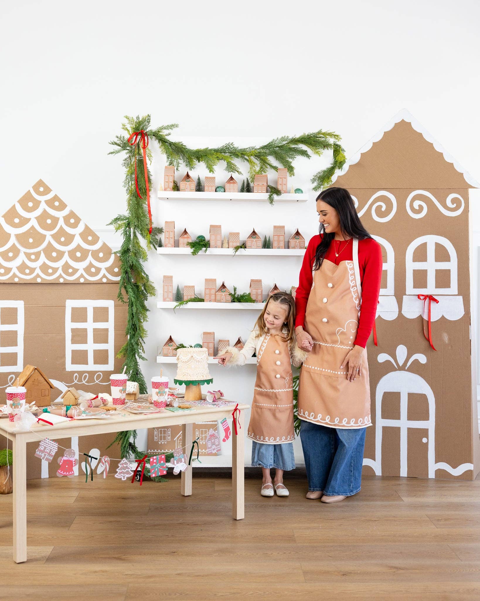 Mother and daughter wearing matching gingerbread aprons at a Christmas baking table surrounded by festive gingerbread decorations.