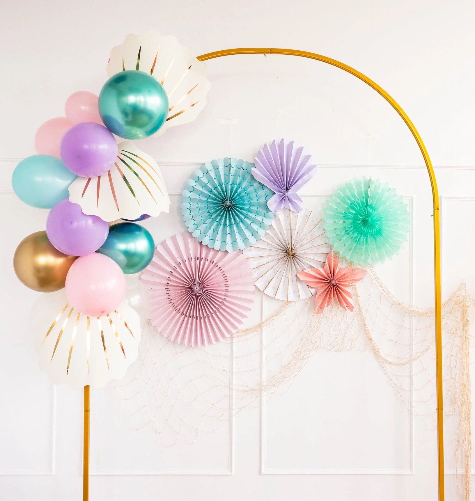 Mermaid-themed party decorations featuring pastel-colored balloons, paper seashells, and ocean-inspired paper fans.