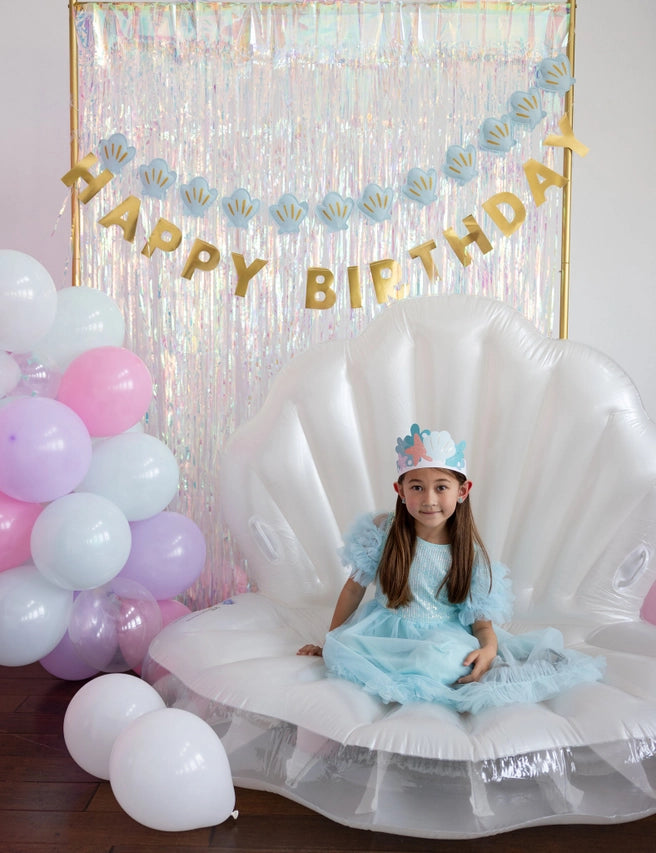 Portrait view of seashell‑and‑gold banner combo above inflatable shell chair and balloon cluster.