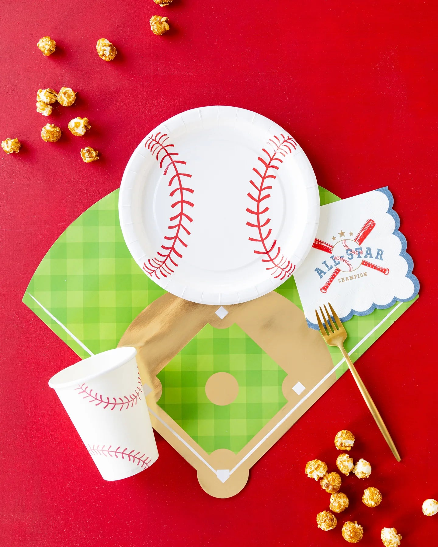 Styled place setting on red backdrop with baseball plate, cup, napkin, and diamond placemat.