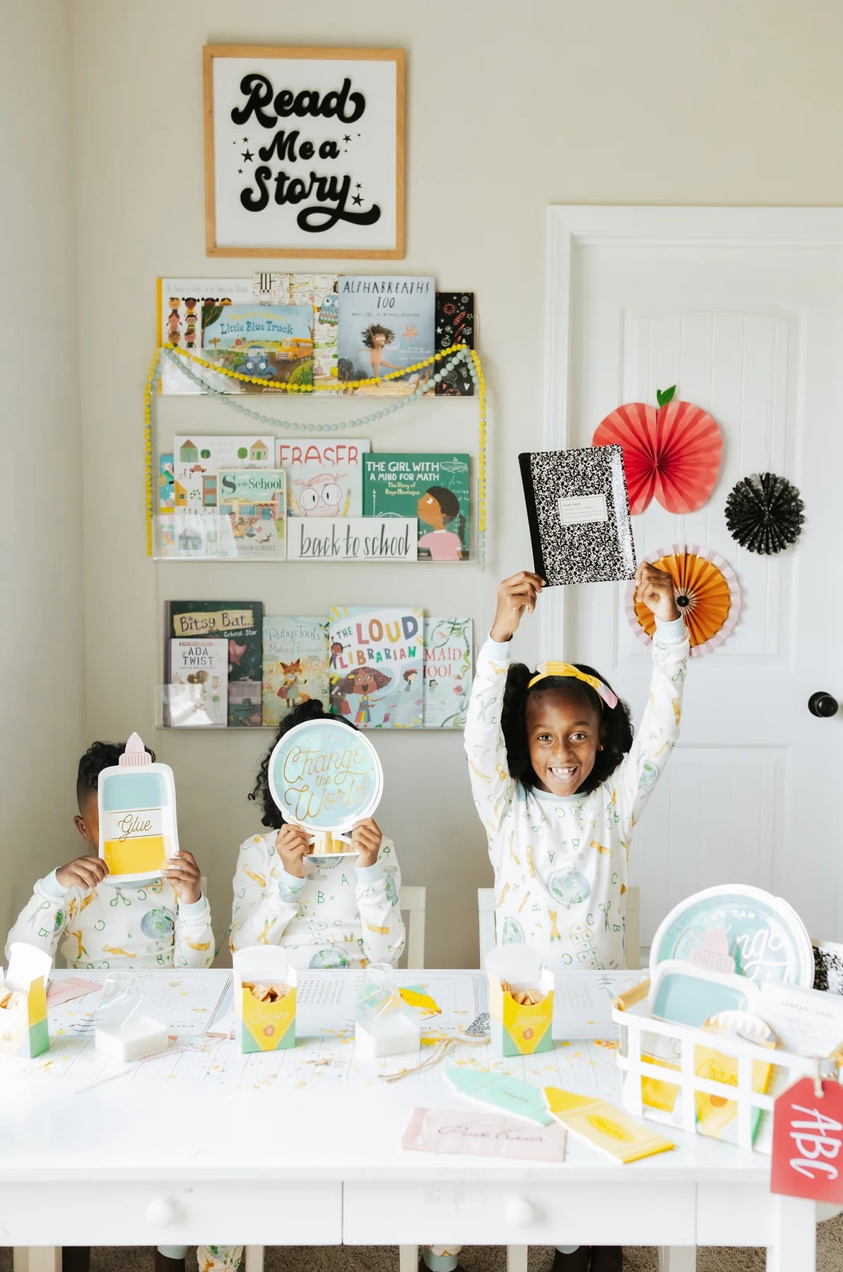 Three kids at a school-themed table setting, one holding the notebook plate above their head