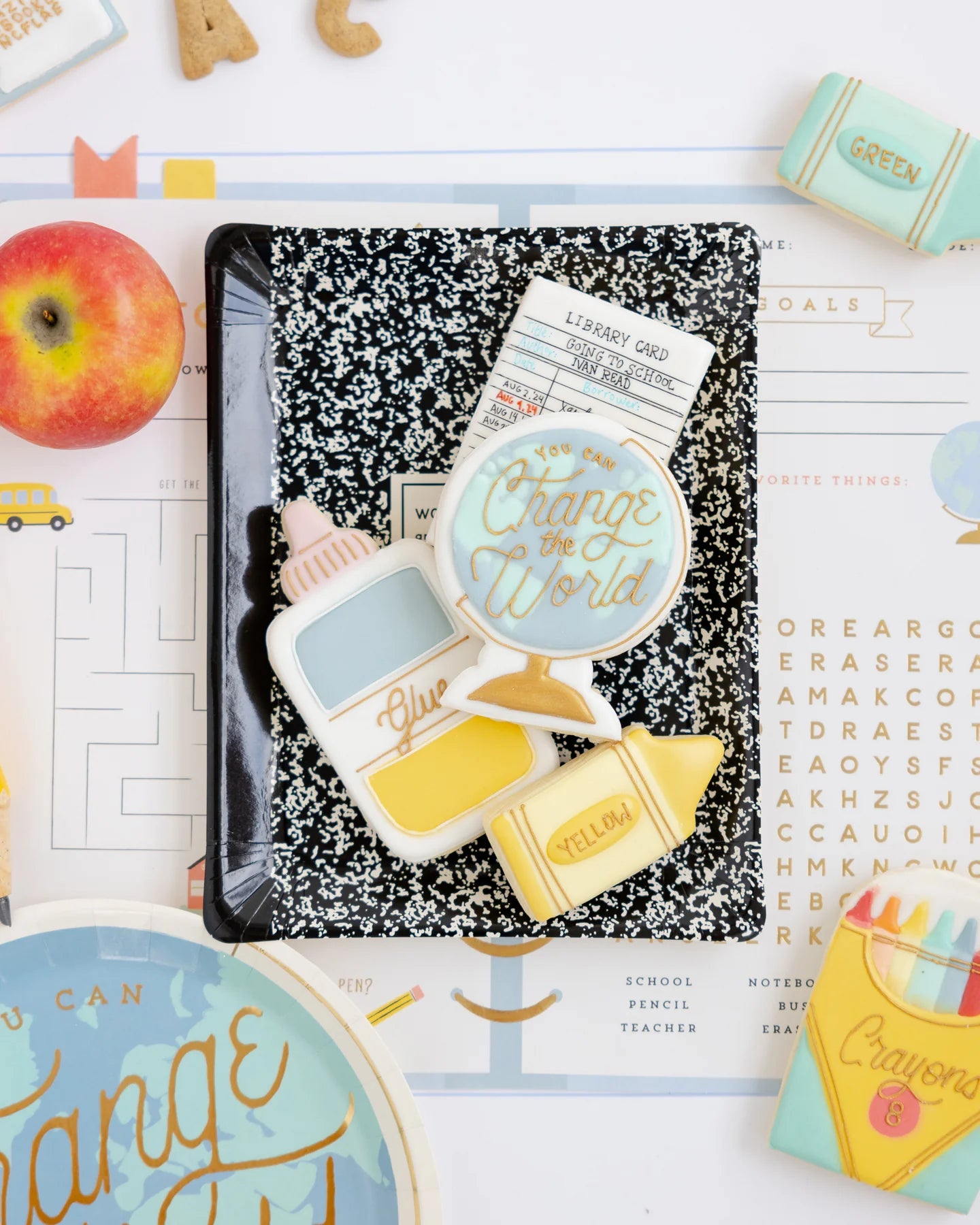 Flat lay of cookies, library card, and themed plates arranged around the composition notebook plate