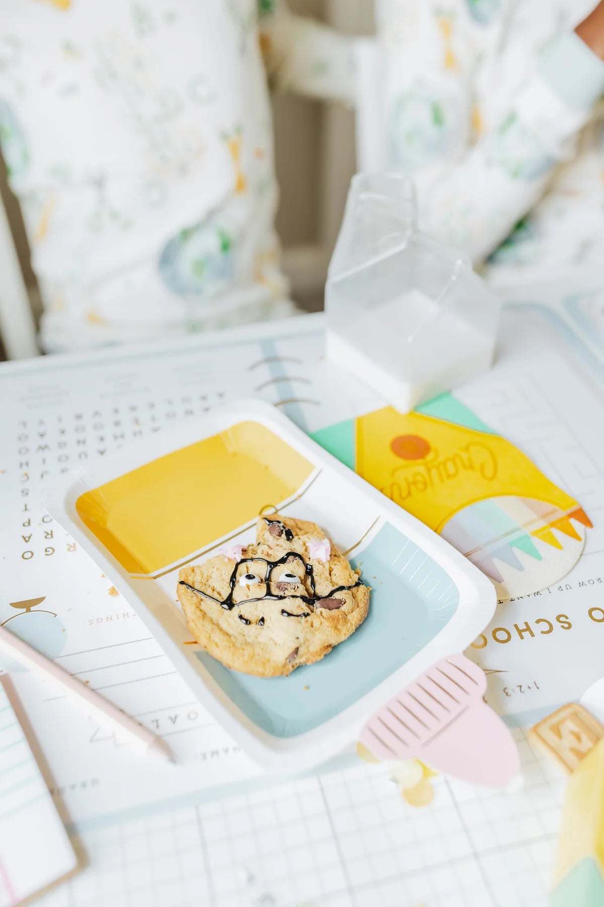 Close-up of cookie decorated with a face on a glue bottle plate, set on a back-to-school placemat.