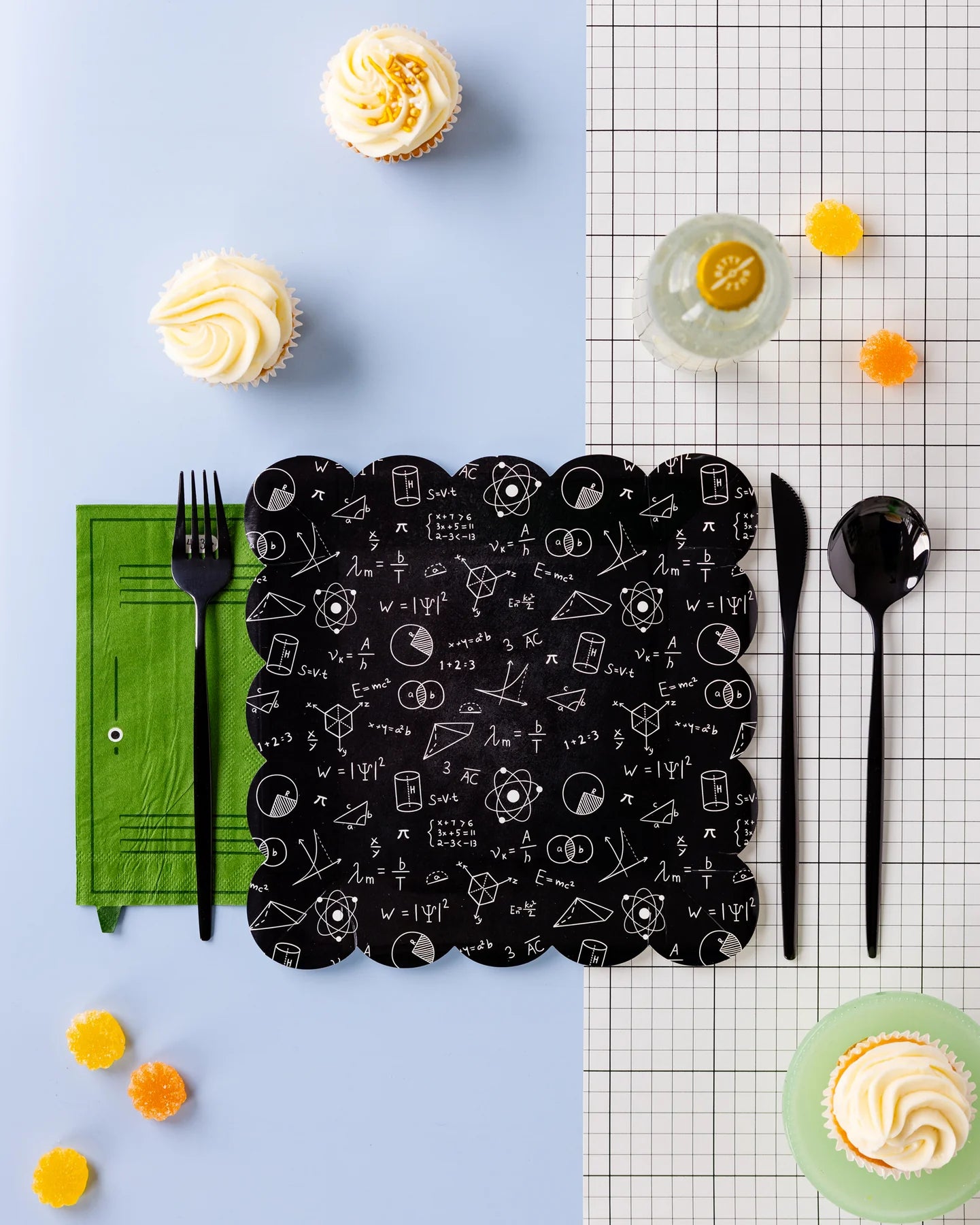 Styled table with black Equations Paper Plate, green napkin, black cutlery, cupcakes, and grid paper as part of a classroom party setup.