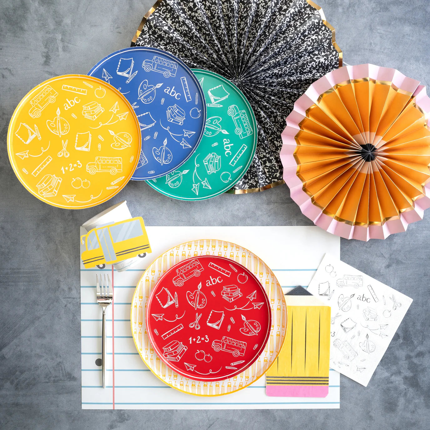 Gray surface styled with yellow pencil dinner plate, red icon plate, and black‑and‑white composition fan.
