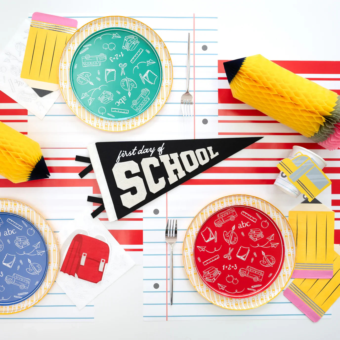 Black‑and‑white striped runner with yellow pencil dinner plate at each place, school bus cup favors nearby.