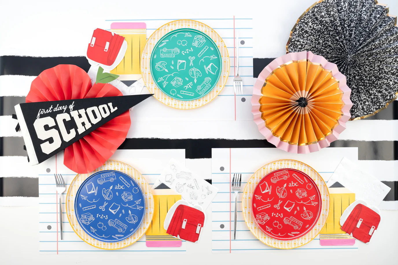 Bold red‑striped runner with layered dinnerware; pencil dinner plate peeks beneath colorful school icon plate.