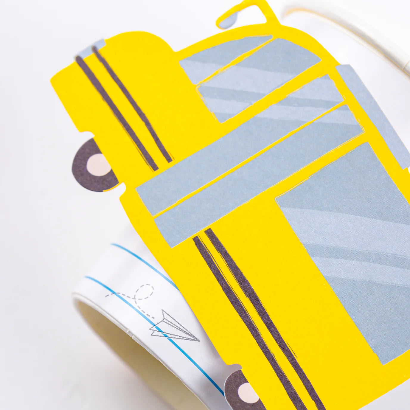 Macro shot of yellow paper school‑bus applique showing window and stripe details attached to ruled‑paper cup.