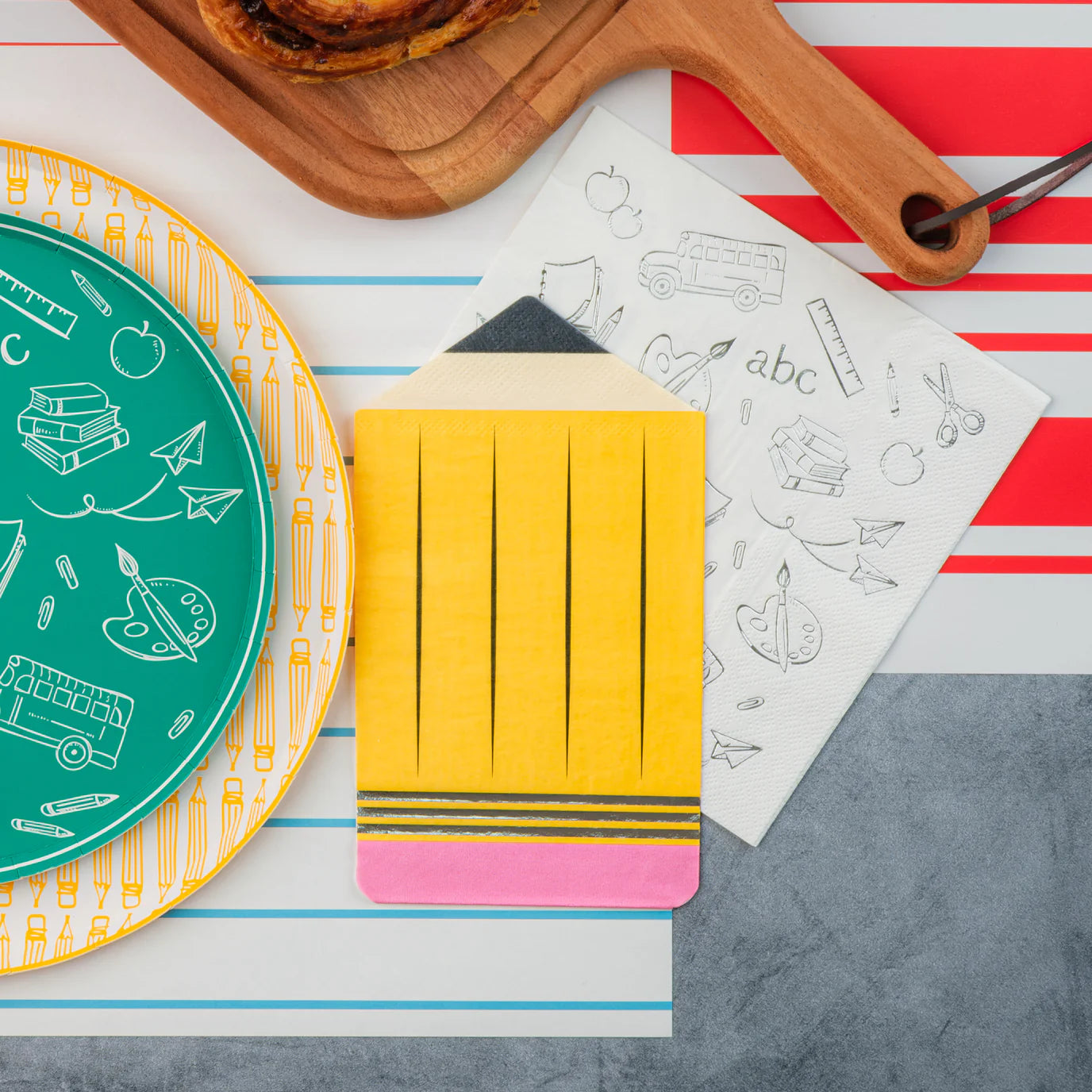 Close view of yellow, red, blue icon dessert plates layered over red‑striped notebook runner.