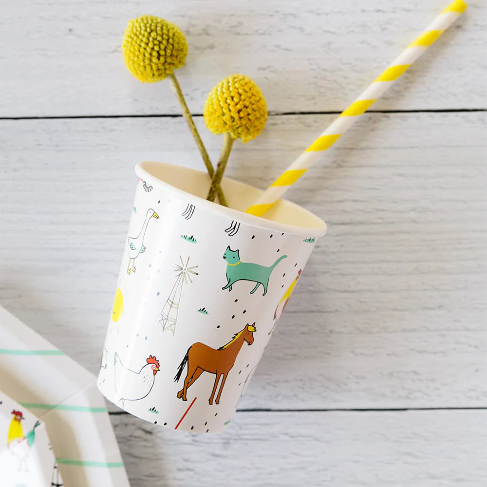 Close‑up of single farm‑print cup holding yellow striped straw and billy ball flowers on white wood surface.