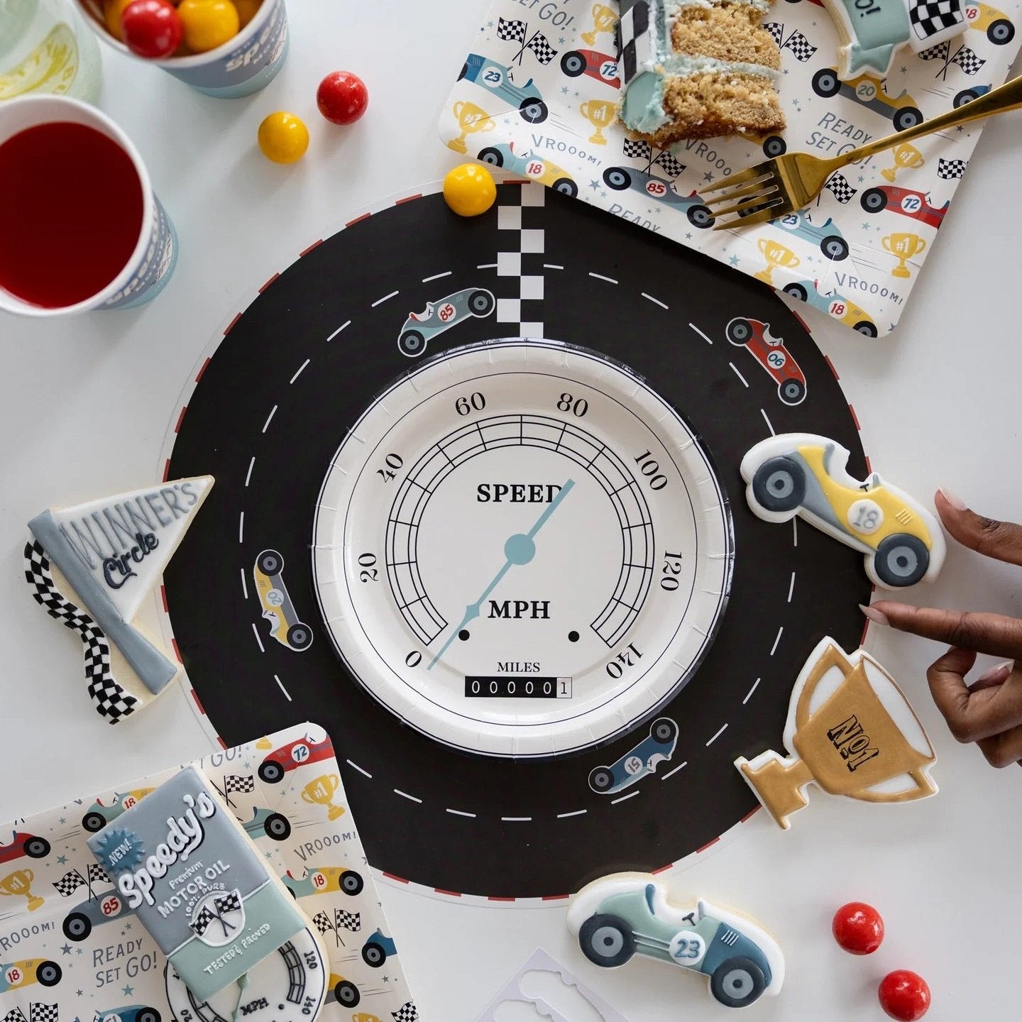 Cars birthday party table featuring speedometer plates, race track decor, and vibrant party treats for a car-themed celebration."