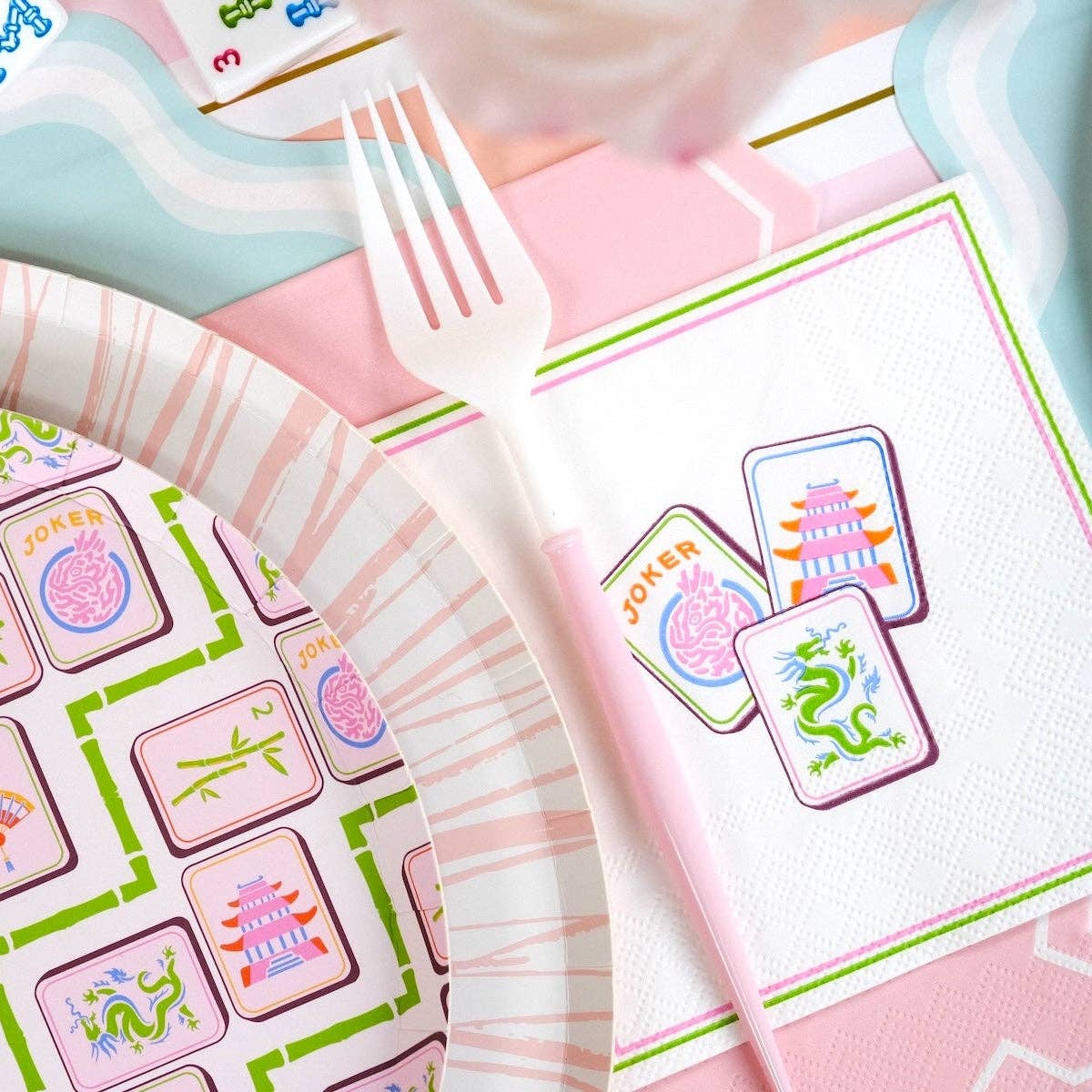 Party supplies including plates, napkins, and a fork with colorful designs on a pink background.