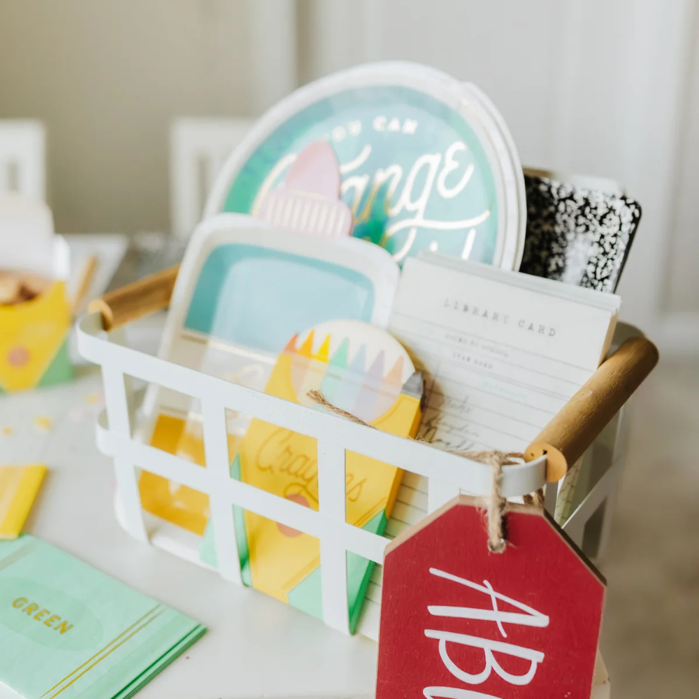 Close-up of a white basket filled with school-themed party supplies, including the crayon box napkins.