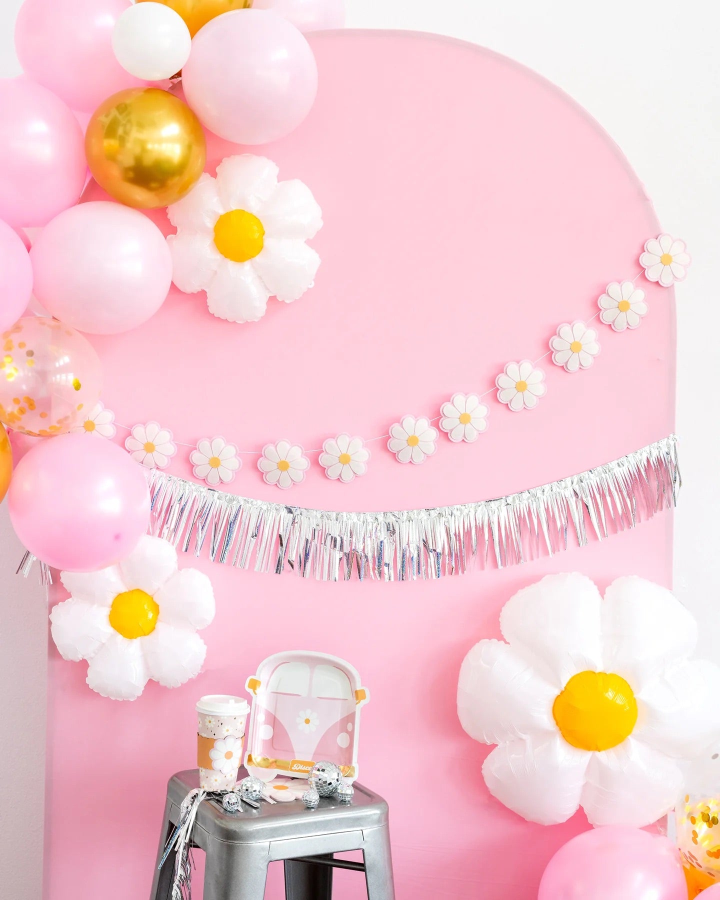 Groovy disco-themed party setup with pink daisy van plates, daisy banner, silver fringe, balloons, and disco balls.