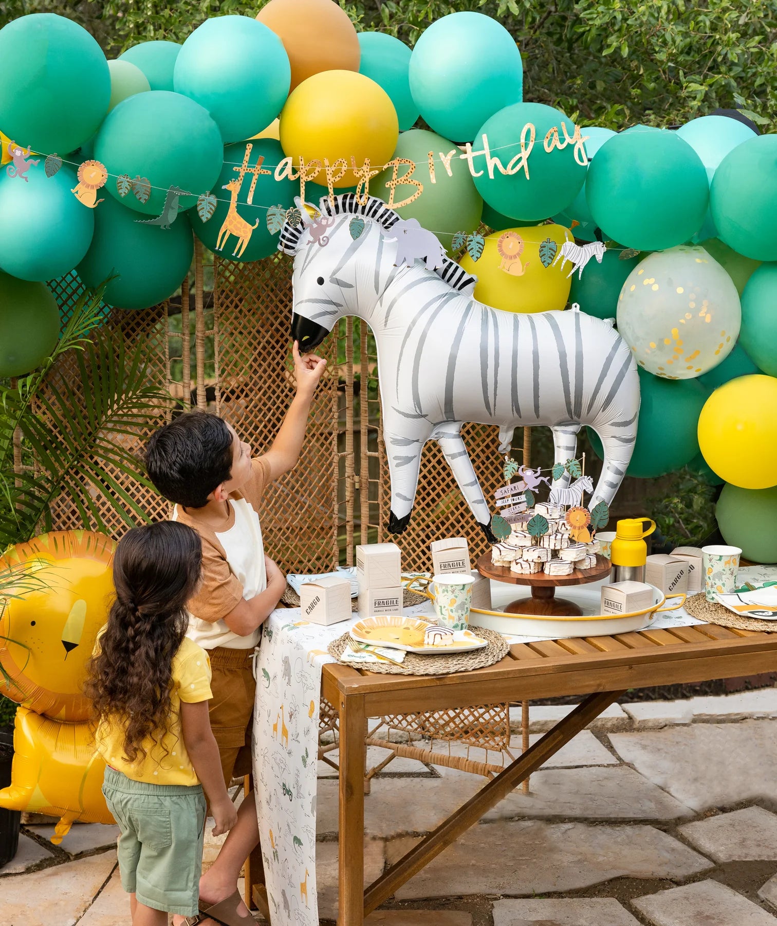 A boy excitedly pointing at a large zebra balloon at a safari-themed birthday party with colorful balloons, animal-themed banners, and safari-inspired table decor.