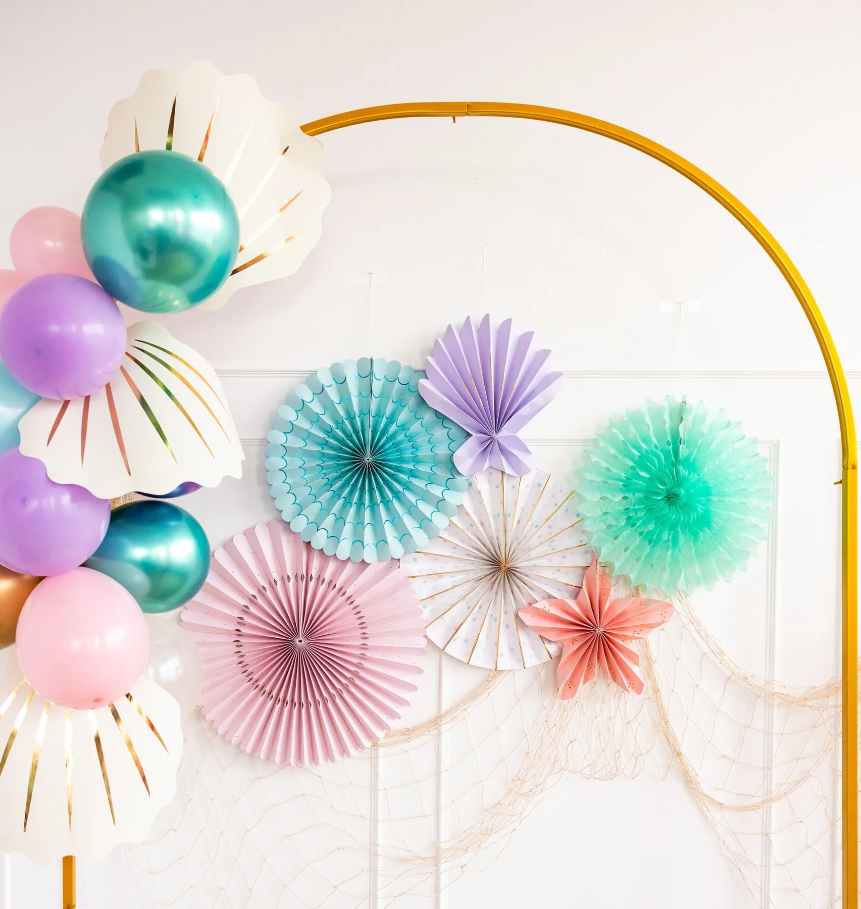 Colorful under-the-sea fan decorations styled above a dessert table with pastel balloons and mermaid-themed party accessories.