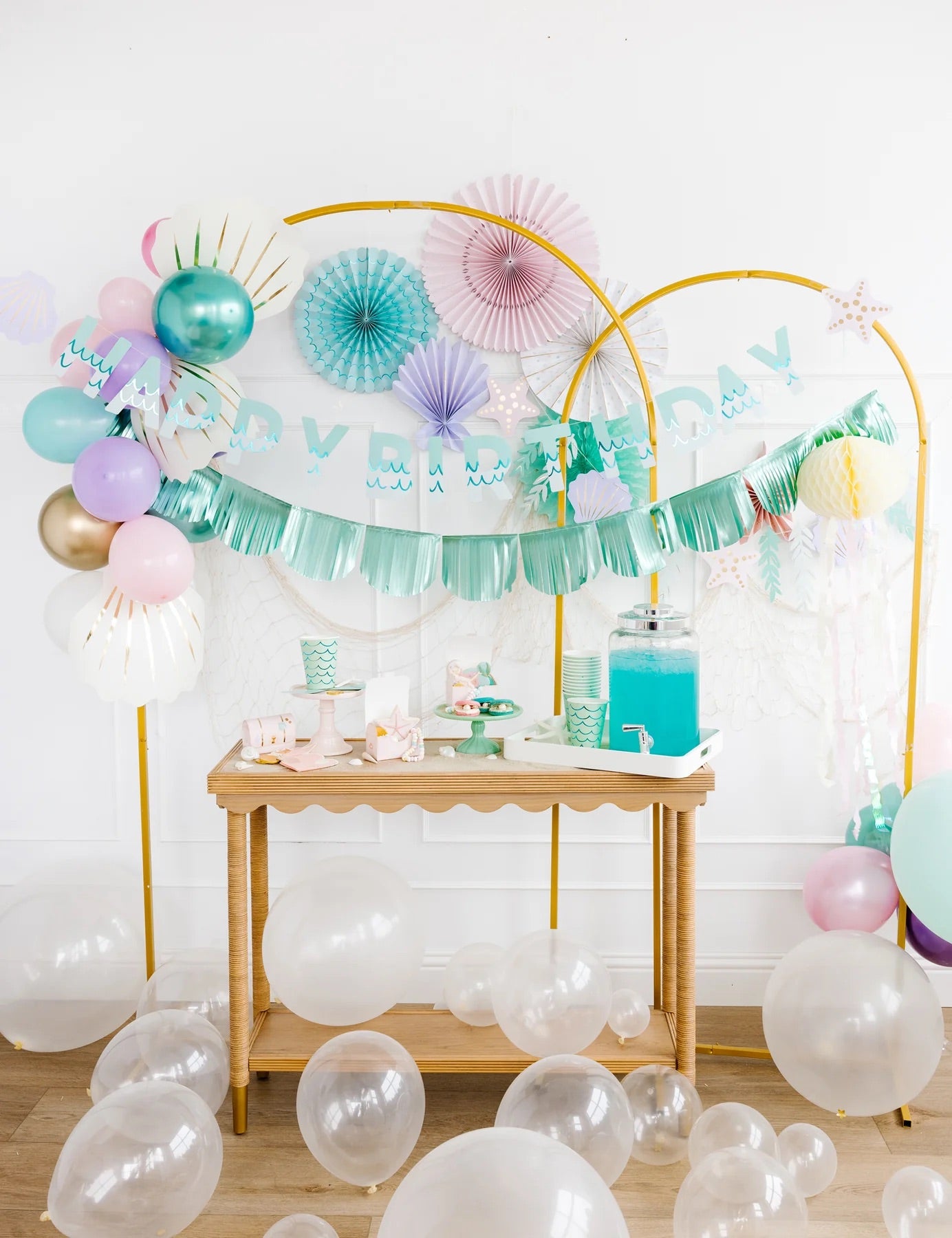 Colorful under-the-sea fan decorations styled above a dessert table with pastel balloons and mermaid-themed party accessories.
