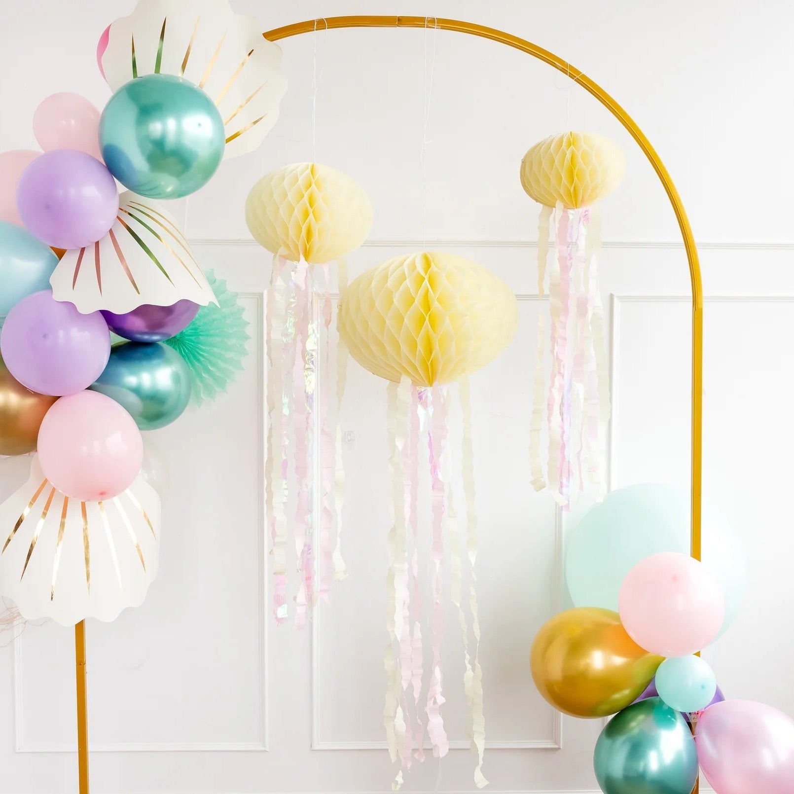 Close-up of pastel honeycomb jellyfish hanging elegantly next to balloon garlands, perfect decor for a mermaid party.