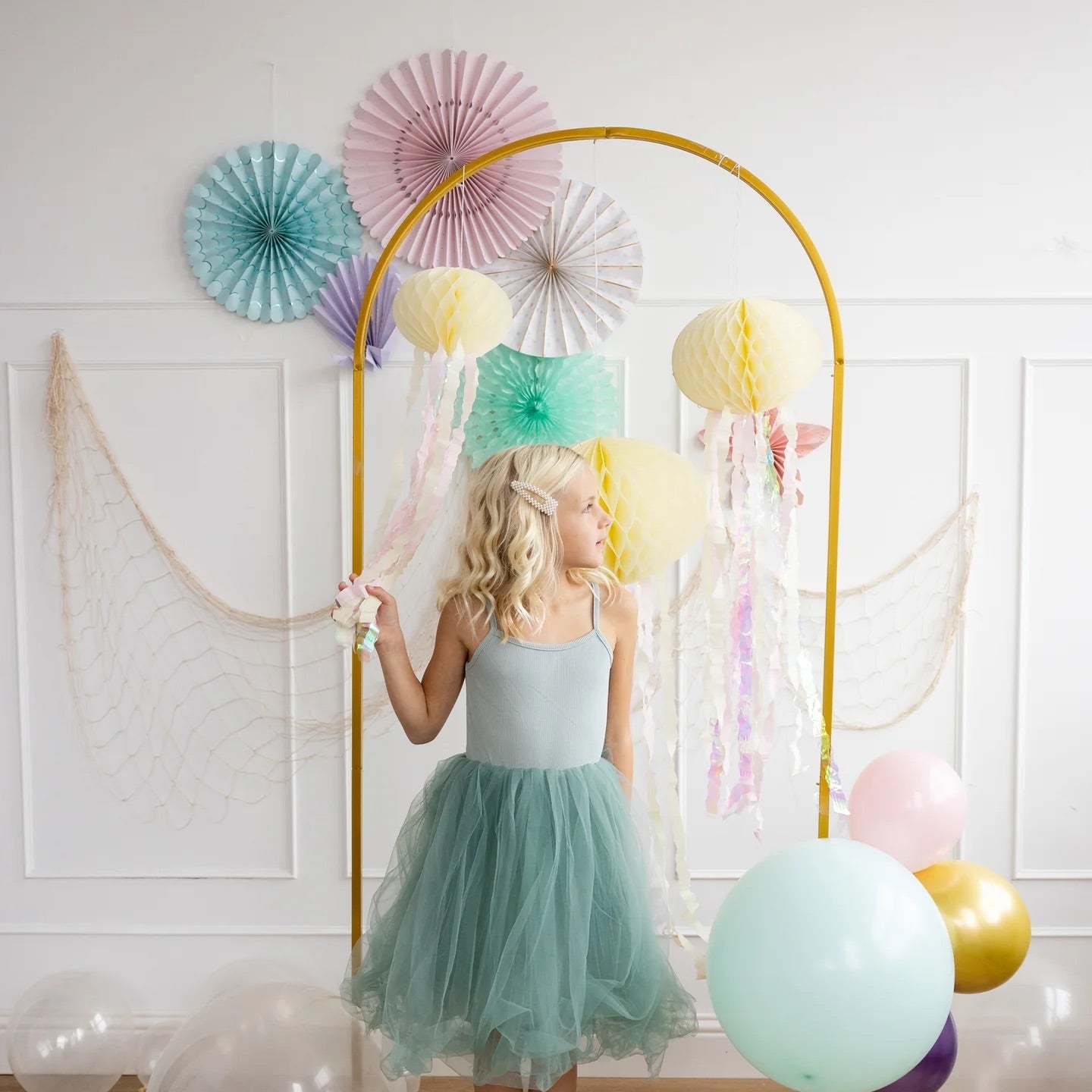 Young girl wearing a teal dress admiring pastel honeycomb jellyfish decor, creating a dreamy mermaid-themed birthday setting.