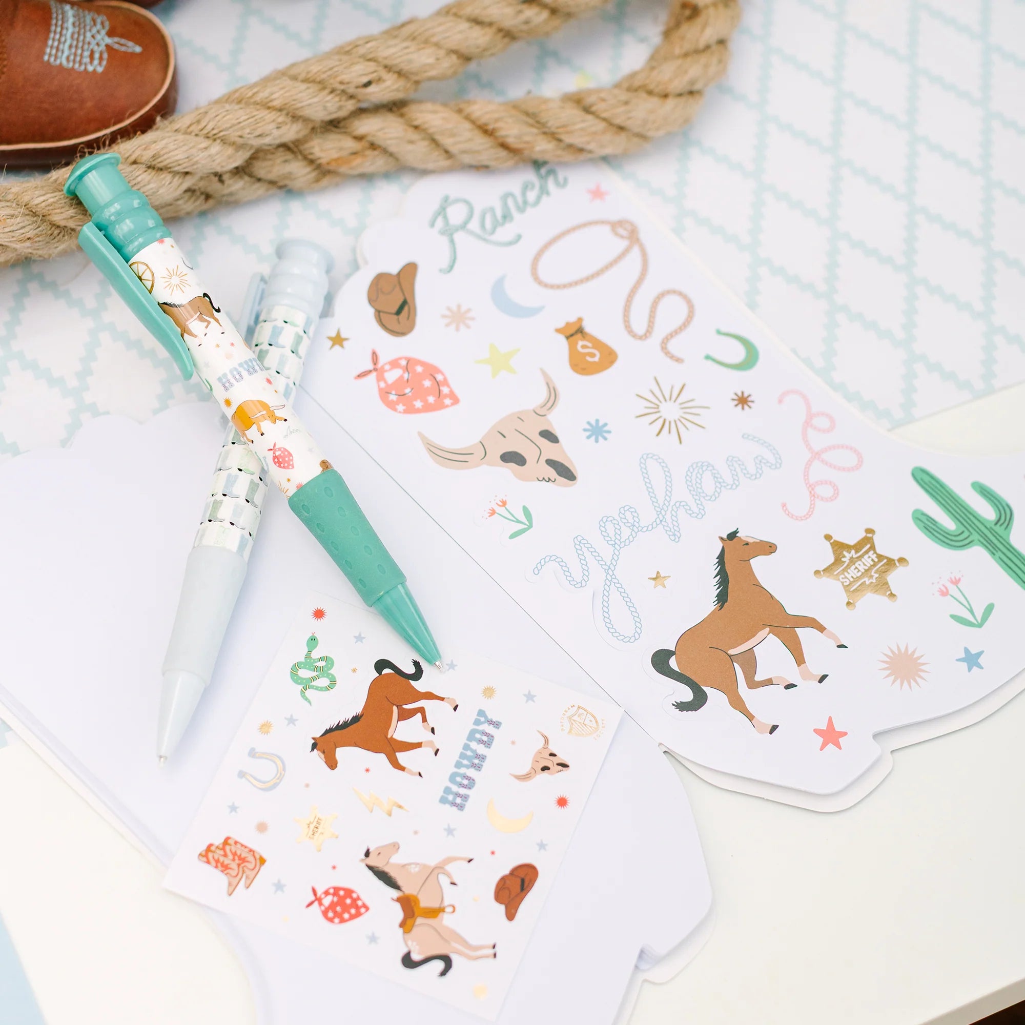 Sticker sheet with rope and pens: Western sticker page and turquoise pen arranged on a pale patterned surface with coiled rope accent.