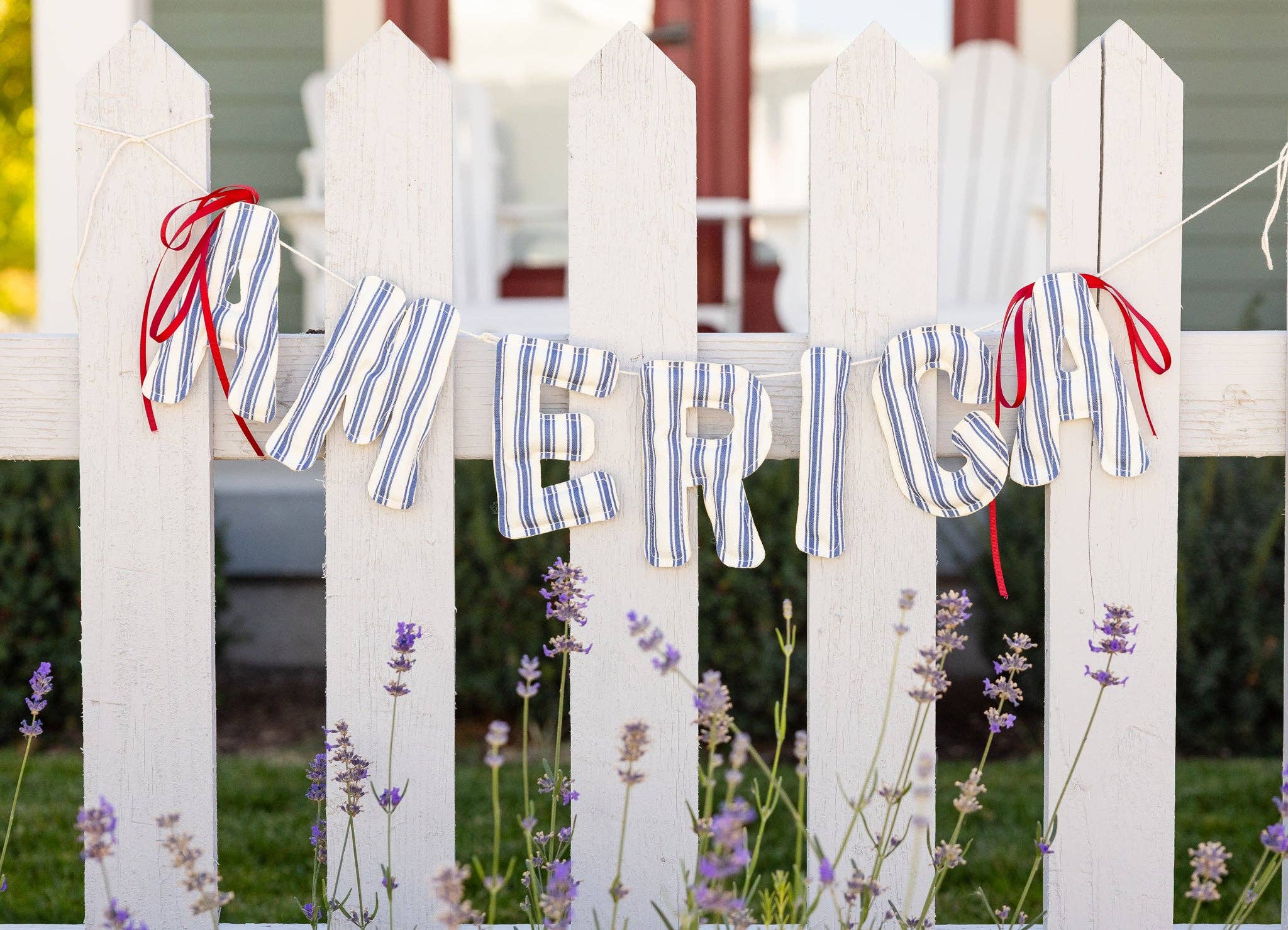 Blue and cream striped America banner hung across white picket fence with lavender below